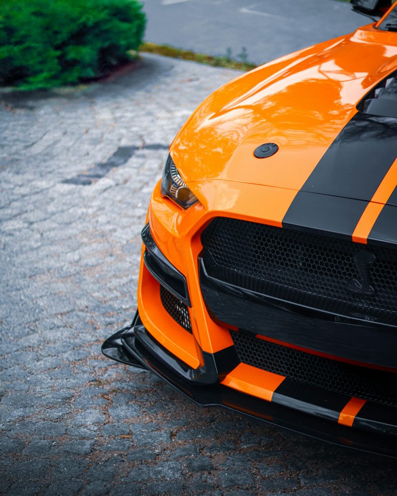Close-up of a striking orange Ford Mustang parked on a stone path with vibrant colors and sleek design.